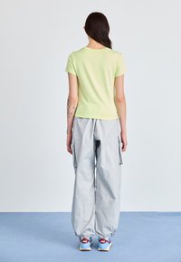 Tricou fitted verde deschis, pantaloni cargo gri cu buzunare și adidași multicolori cu branding proeminent. Design simplu, croială lejeră.