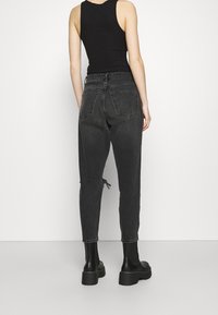 Top negro sin mangas combinado con jeans de cintura alta, sueltos, de color gris oscuro, que cuentan con dos bolsillos traseros y detalles desgastados en los tobillos. Botines negros.