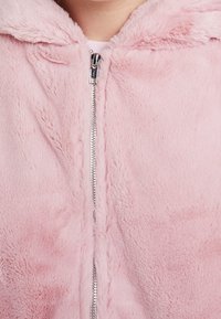 Rosa fuskpälsjacka med dragkedja som har en mjuk textur, huva och metallisk dragkedja. Slät tyg med en mysig look och minimala sömmar.