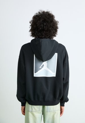 Black hoodie with a large white graphic of a jumping figure on the back. Features a drawstring hood and ribbed cuffs. Soft fabric texture.