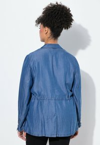 Denimjacka i ljusblått, med krage, insydd midja, långa ärmar och knappade manschetter. Slät textur med avslappnad passform.