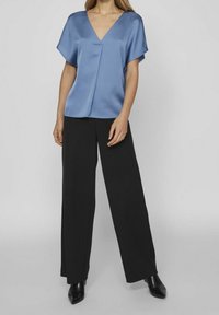 Haut en satin bleu avec un décolleté en V et des manches courtes, assorti à un pantalon large noir et des chaussures noires à talons pointus. Texture lisse et coupe ample.