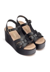 Sandales à plateforme noires avec un design de bride tressée, une semelle intérieure douce couleur tan et une fermeture à boucle. Présente un talon compensé noir texturé.