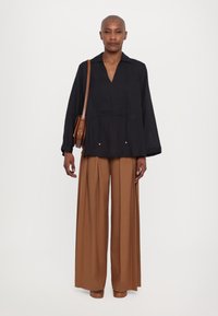 Camicia nera a maniche lunghe con scollatura a V, abbinata a pantaloni marroni a gamba larga. Borsa a tracolla marrone con spallaccio e hardware minimale.