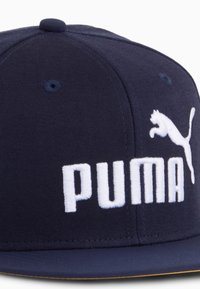 Sötétkék, lapos karimájú, szövetből készült sapka, amelyen kiemelt, fehér hímzés látható, rajta a "PUMA" felirattal és egy ugró pumát ábrázoló logóval.