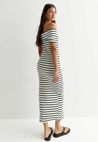 Svart- och vitrandig off-shoulder maxiklänning med korta ärmar, figurnära silhuett och en slits på sidan; ihop med svarta flip-flops.