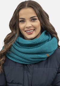 Sciarpa infinity in maglia color teal con un motivo testurizzato e uno strato superiore liscio, arricchita da un piccolo tag in pelle, avvolta attorno al collo.