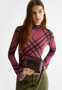 Borsa a tracolla bordeaux con una finitura textured, hardware ovale e una tracolla removibile. Indossata con un top aderente a fantasia rosa.