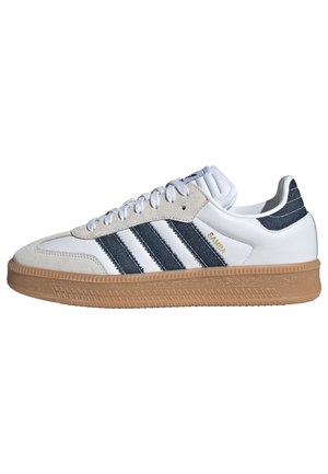 Hvid sneaker med sorte striber, beige ruskind detaljer og gummisål, vist fra siden mod en hvid baggrund.