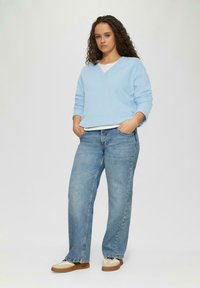 Lichtblauwe gebreide trui met een v-hals en lange mouwen, gecombineerd met blauwe denim wijd uitgesneden jeans en tan- en witte sneakers.