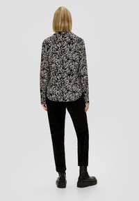 Maglietta nera a maniche lunghe con un motivo astratto bianco, abbinata a pantaloni in velluto a coste neri e stivali neri chunky alla caviglia.