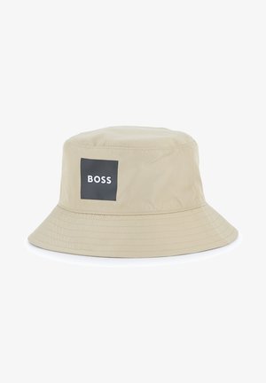 Chapeau bob beige en tissu avec un large bord et une calotte ronde. Il comporte un patch rectangulaire noir avec le texte "BOSS" en blanc.