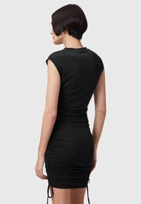 Svart figursydd klänning i stretchmaterial. Har ärmar med kort ärm, rynkade detaljer längs sidorna och dragskoaccenter vid fållen.