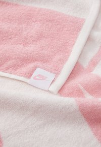 Růžový a bílý froté ručník se čtvercovým vzorem, s bílým okrajem a malou růžovou nášivkou loga Nike na okraji.