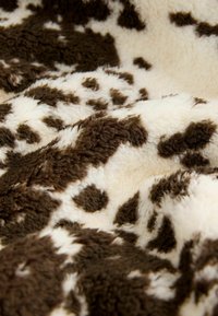 Faux fur deken met een bruin en crèmekleurig koeienprintpatroon. Zachte textuur met variërende lengtes van de vacht. Ovale en onregelmatige vlekken.