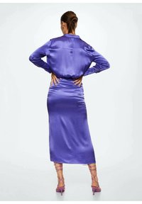 Violet satiini mekko, jossa on tiukka vyötärö ja pitkät hihat, yhdistettynä vaaleanpunaisiin remmissandaaleihin. Sujuva rakenne, virtaava muotoilu, elegantti siluetti.