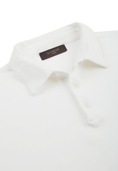 Polo shirt bianco con colletto e tre bottoni, e un'etichetta nera con la scritta "SLOWEAR ZANONE" all'interno del colletto.