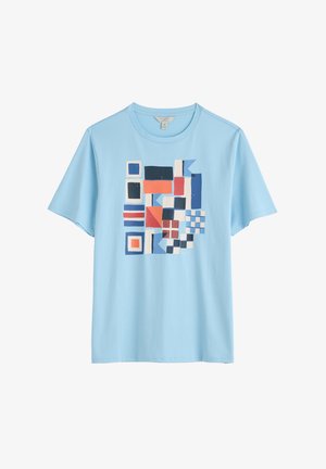 T-shirt en coton bleu clair avec un imprimé géométrique multicolore comportant diverses formes, y compris des carrés et des rectangles en bleu, rouge et blanc.