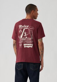 Bordeauxfarvet bomulds-t-shirt med grafisk tekst og illustrationer på ryggen, herunder et stort bogstav "A" og Levi's logoet.
