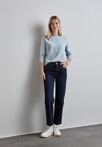 Maglione azzurro chiaro a maniche lunghe abbinato a jeans scuri e sneakers bianche. La texture è morbida, con una vestibilità rilassata e dettagli a costine sui polsini.