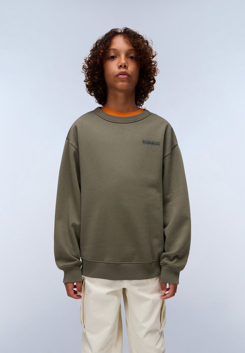 Sudadera verde oliva con cuello redondo y puños de canalé, que presenta un pequeño logotipo impreso en el pecho, llevada sobre una camisa naranja.