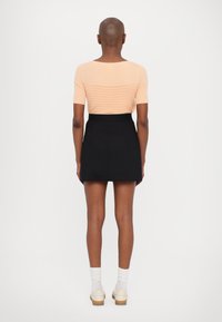 Perzikkleurig geribbeld gebreid topje met korte mouwen, gecombineerd met een zwarte high-waisted rok. Witte enkel sokken en lichtgekleurde schoenen worden gedragen.