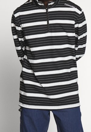 Schwarz-weißer gestreifter Langarm-Quarter-Zip-Oberteil aus weichem Material mit gesticktem Logo am Kragen. Details umfassen seitliche Schlitze.