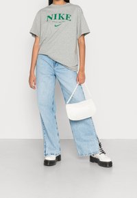Camiseta de manga corta gris de Nike con logo verde, vaqueros de pierna ancha azul claro, bolso blanco con asa de cadena y botas de plataforma blancas gruesas.