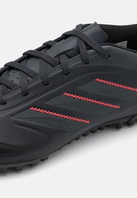 Black soccer shoe with a textured leather upper, featuring three red zigzag stripes and a durable rubber sole with studs for traction.