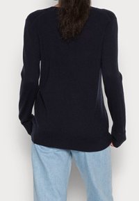 Marinblå stickad tröja med långa ärmar, rund hals och ribbade mudd. Kombinerad med ljusblå, avslappnade jeans. Slät textur, minimalistisk design.