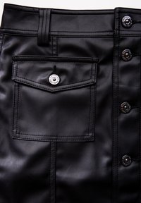 Svart fusk läderkjol med en bakficka, silverfärgade tryckknappar och synliga sömdetaljer. Slät textur med en figurnära design.