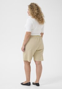 Shorts rayés beiges avec une taille élastique, en tissu léger, associés à un haut ajusté blanc et des ballerines noires.