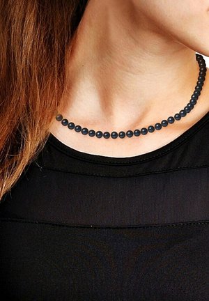 Collier en perles noires composé de perles sphériques uniformes de différentes tailles, exposé sur un cou avec un fond noir.