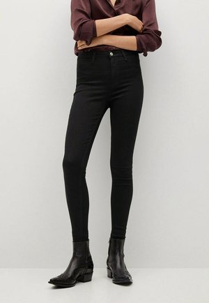 Jeans negros ajustados que presentan una cintura alta, un corte slim y un diseño minimalista. Combinados con botas de cuero negras con detalles bordados.