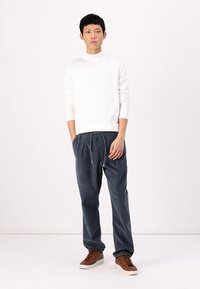 Suéter blanco de manga larga con cuello alto simulado, combinado con pantalones de pana sueltos de color azul oscuro y zapatos marrones con cordones. Ajuste simple y relajado.
