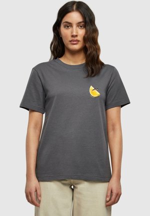 Graues Baumwoll-T-Shirt mit kurzen Ärmeln, das auf der linken Brust eine kleine gestickte gelbe Zitronenscheibe zeigt. Runder Ausschnitt, lockere Passform.