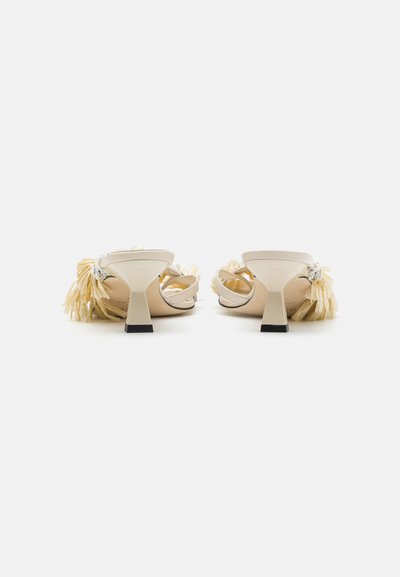 Beige heeled mules with a back strap, featuring a textured sole and decorative light-colored tassels on the side.