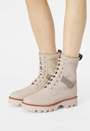 Stivaletti beige stringati alla caviglia con tomaia testurizzata, suola in gomma e battistrada spesso. Presentano un pannello in rete e un tassello sul retro.