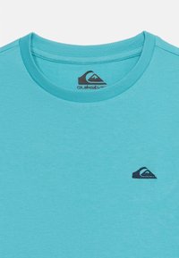 Τιρκουάζ μπλουζάκι με στρογγυλή λαιμόκοψη και μικρό μαύρο λογότυπο Quiksilver κεντημένο στην αριστερή πλευρά του στήθους και τυπωμένο στο εσωτερικό της περιοχής του λαιμού.