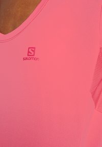 Pink athletic shirt with a V-neck and textured fabric. Features a small "Salomon" logo on the chest. Short sleeves with a breathable design.
