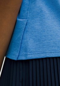 Top atletico blu con texture e spacchi laterali, abbinato a una gonna nera plissettata. Presenta un tessuto morbido e dettagli di orlo cuciti.