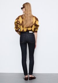 Dżinsy w ciemnym kolorze, dopasowane, w połączeniu z brązowym i żółtym swetrem w romby. Gładka tekstura z wyraźnym krojem.