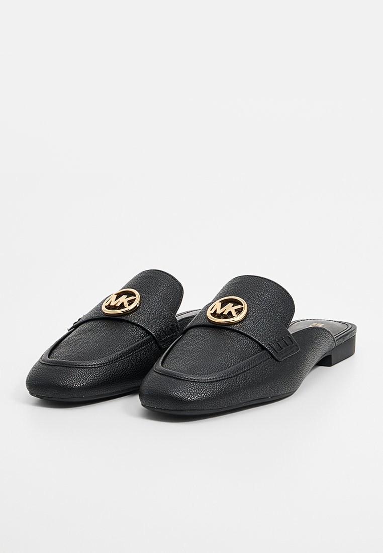 Zwarte leren instappers met een gestructureerd oppervlak, puntige neus en gouden MK-logo op de bovenkant. Platte zool.