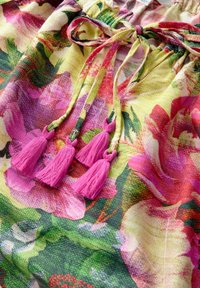 Bloemenpatroonstof met tinten van geel, roze en groen, met roze franjes aan een trekkoordsluiting. Gelaagd, lichtgewicht materiaal.