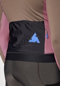Kortærmet cykeltrøje i brun og pink, med en sort mesh-lomme med et blåt logo, samt en slank, tætsiddende torso og buks-design.