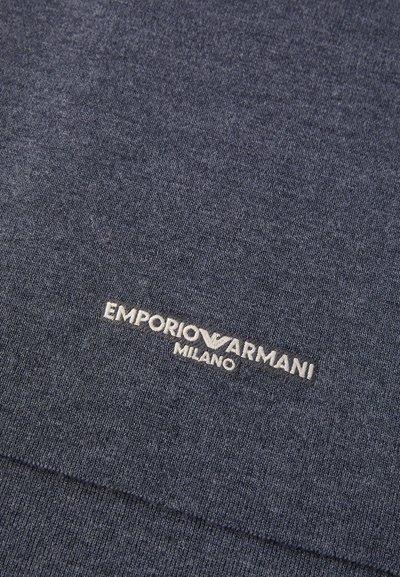 Tumši zila adīta auduma, ar baltu izšūtu logo "EMPORIO ARMANI MILANO" apakšā. Mīksta tekstūra, vienkāršs dizains.