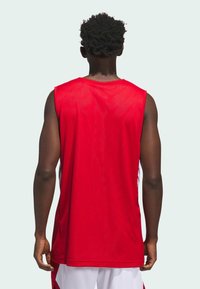 Rød ærmeløs sportsjersey lavet af åndbart stof, med en løs pasform, der har hvide sideaksenter og en glat tekstur.