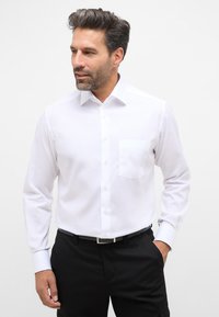Witte long-sleeve overhemd met een puntige kraag, enkele borstzak en een soepele textuur, gecombineerd met zwarte broeken en een riem.