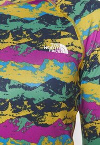 Farverig langærmet termisk top med et multicolor bjergmønster i blå, grøn, gul og pink samt et hvidt logo på brystet.