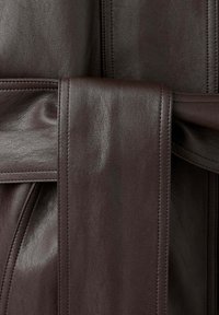 Gros plan d'un tissu en cuir marron foncé avec des coutures détaillées et une large ceinture enroulée autour du matériau.